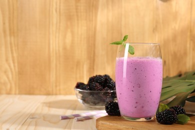 Delicious blackberry smoothie in glass and berries on wooden table, space for text