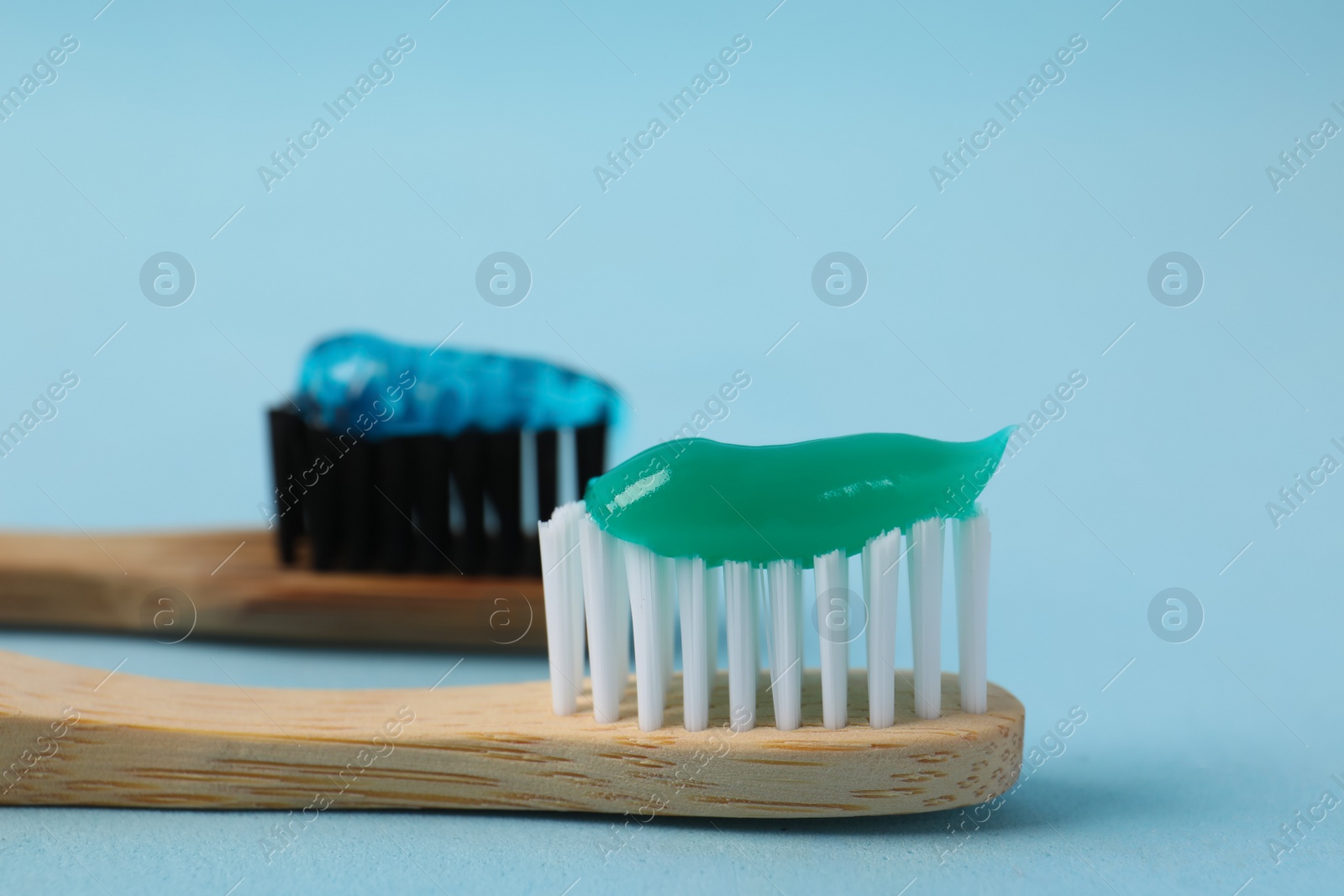 Photo of Wooden brushes with toothpaste on light blue background, closeup