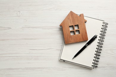 Photo of Mortgage concept. House model, notebook and pen on white wooden table, top view with space for text