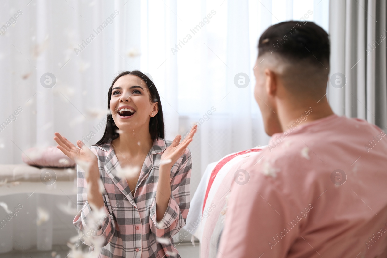 Photo of Happy couple having fun with flying feathers after pillow fight in bedroom