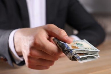 Photo of Money exchange. Man holding dollar banknotes at wooden table, closeup