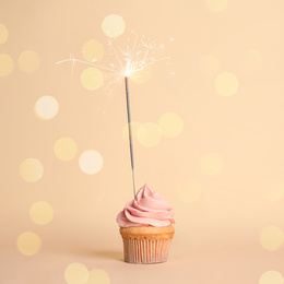 Image of Birthday cupcake with sparkler on beige background