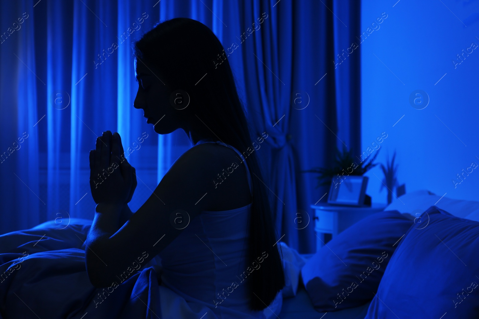 Photo of Young woman praying in dark room at night. Bedtime