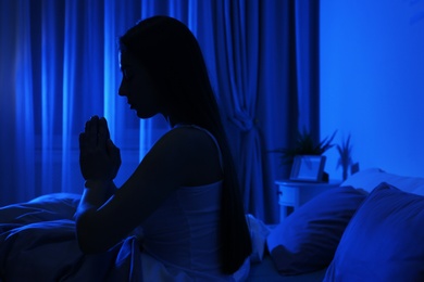 Young woman praying in dark room at night. Bedtime