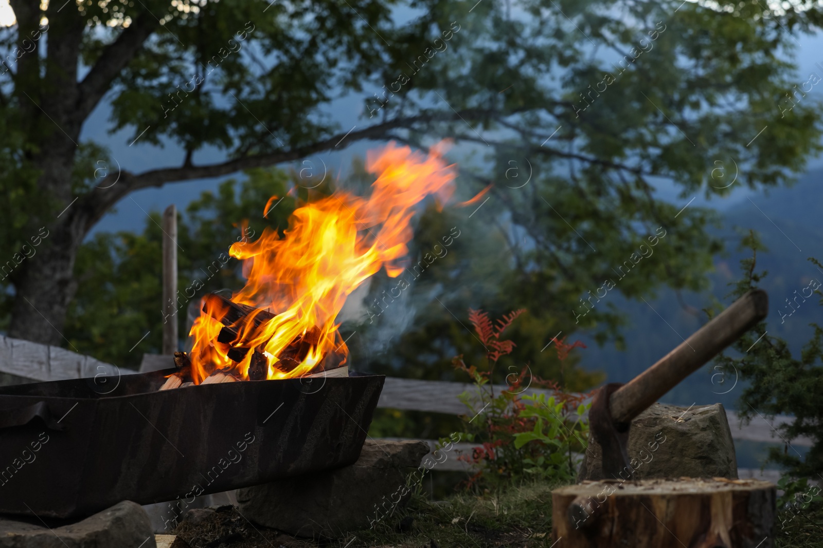 Photo of Metal brazier with burning firewood on backyard in mountains