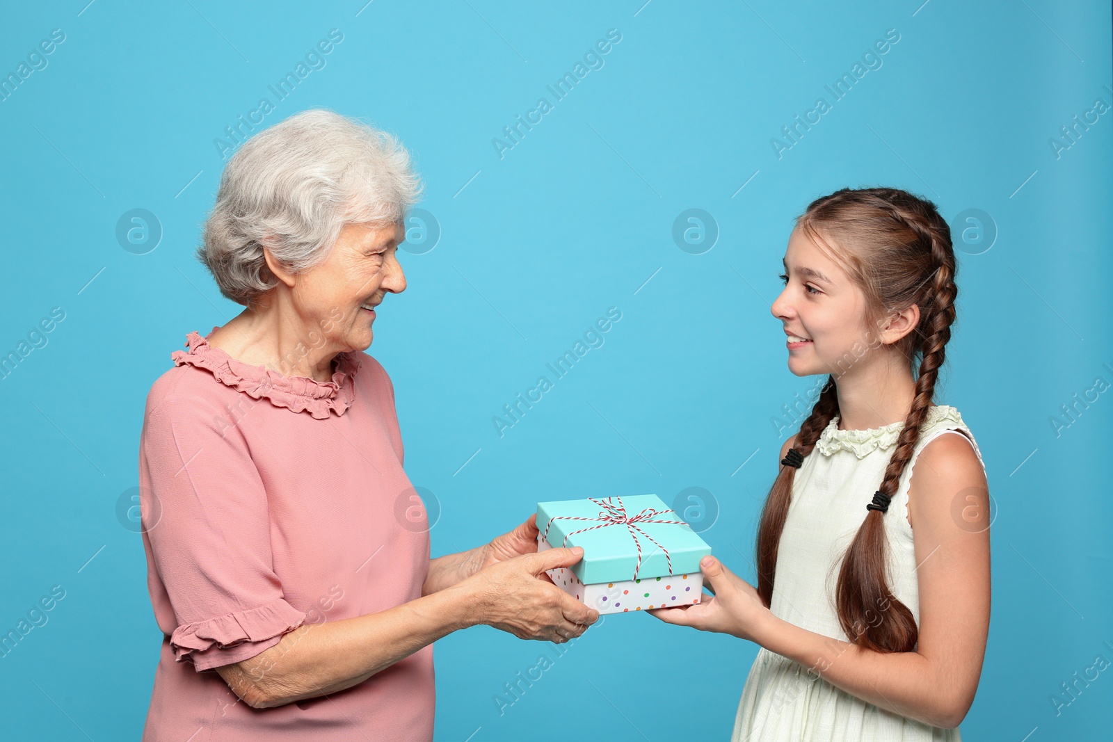 Photo of Cute girl congratulating her grandmother on light blue background