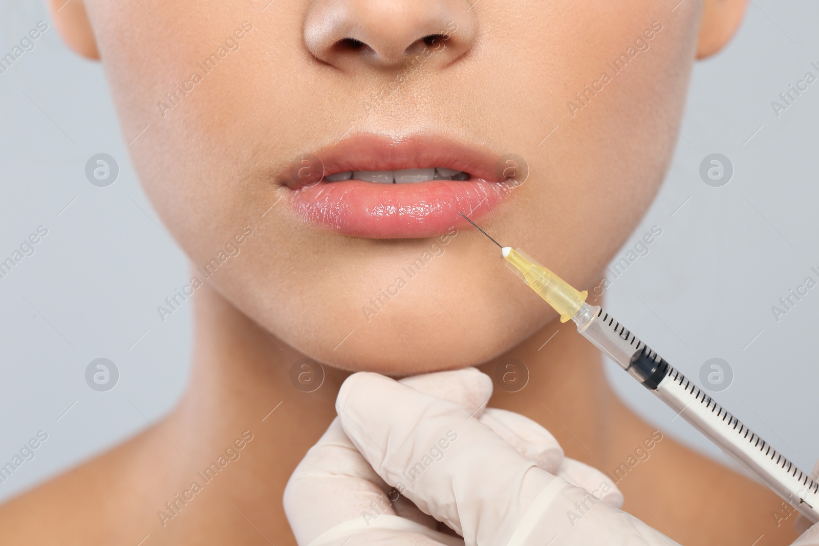 Photo of Young woman getting lips injection on grey background, closeup. Cosmetic surgery