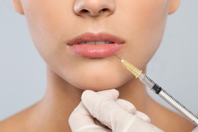 Young woman getting lips injection on grey background, closeup. Cosmetic surgery