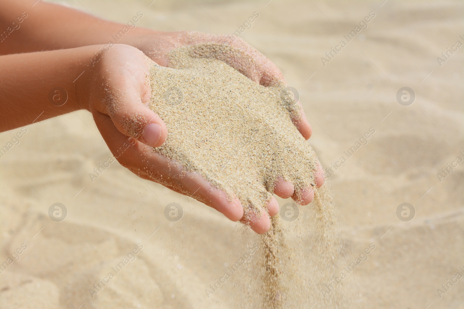 Photo of Child pouring sand from hands on beach, closeup. Fleeting time concept