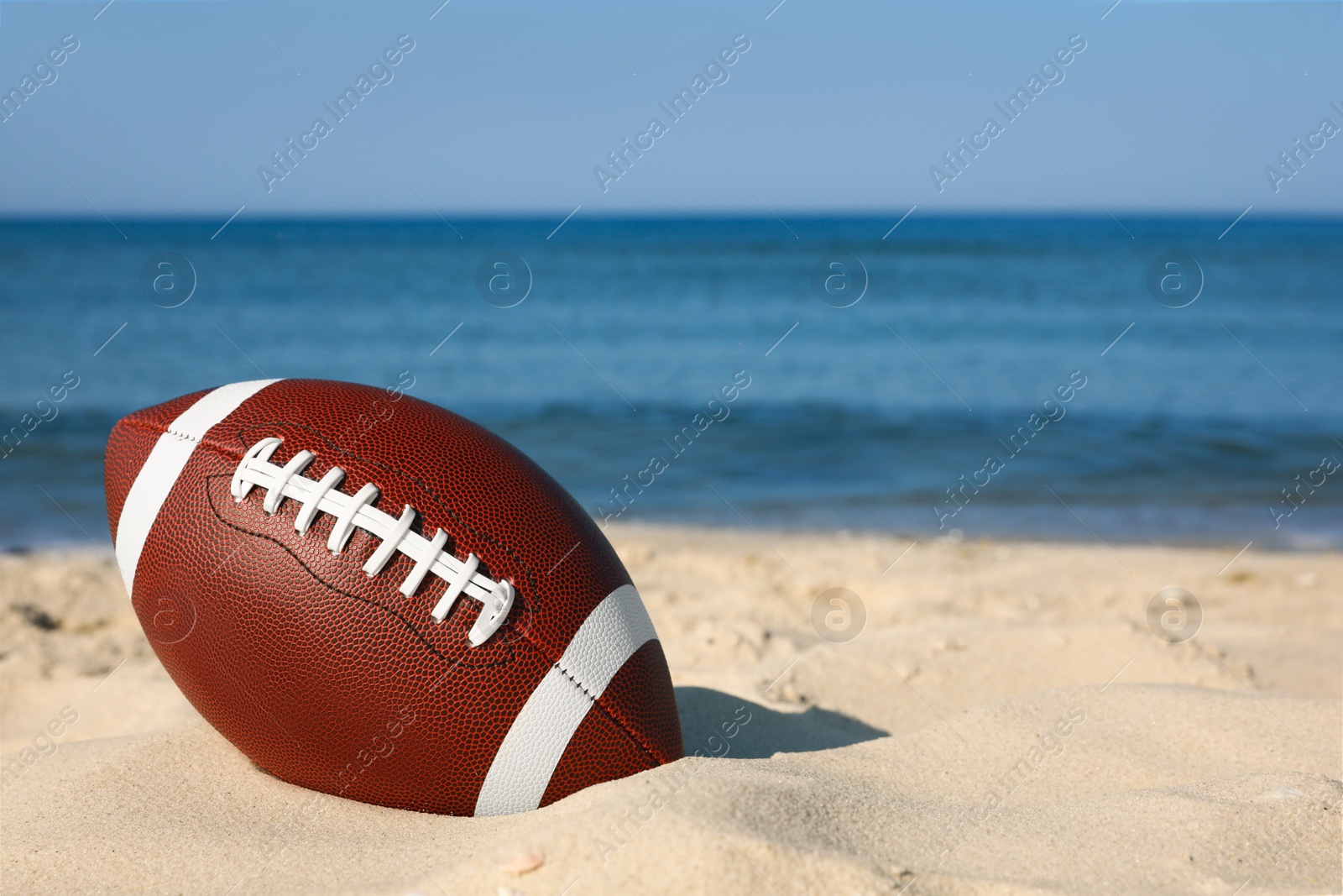 Photo of American football ball on beach. Space for text