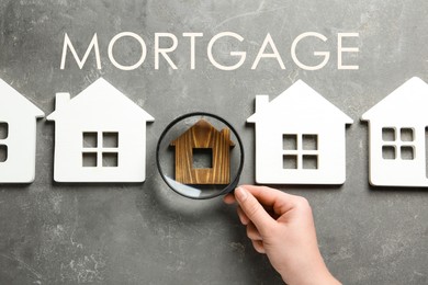 Image of Mortgage concept. Woman with magnifying glass and different house models on grey stone background, top view