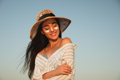 Photo of Happy young woman with sun protection cream on face against blue sky