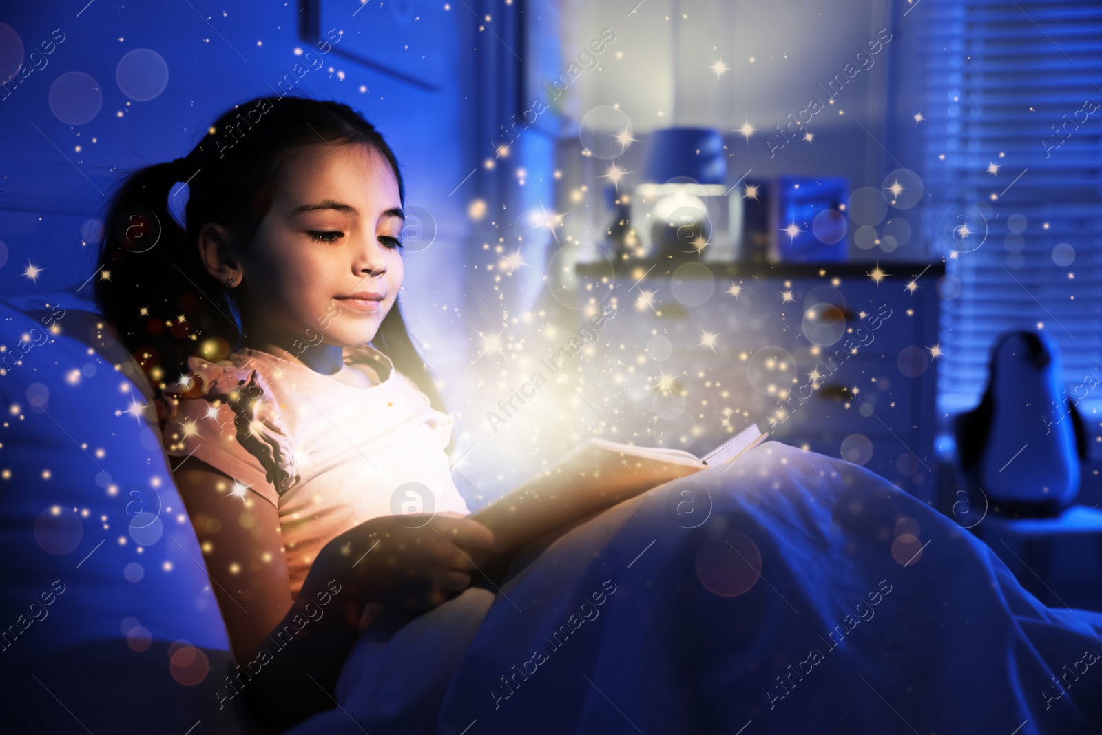 Image of Little girl reading fairy tale in dark bedroom