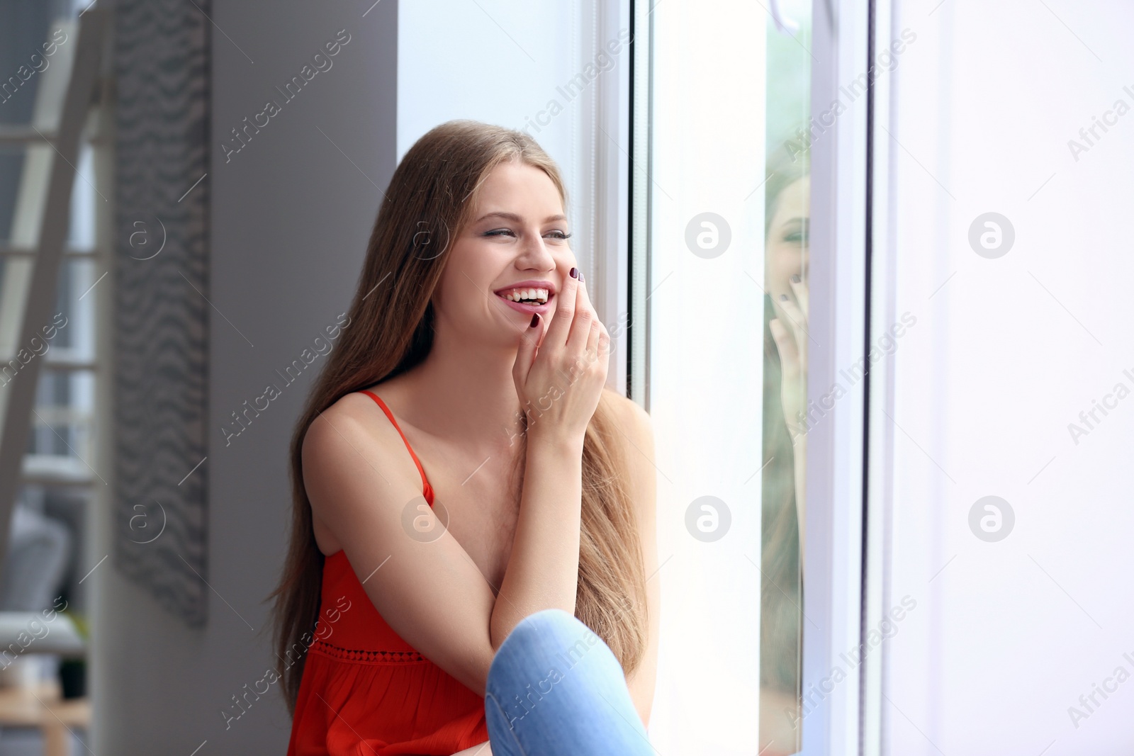 Photo of Young happy woman sitting near window at home