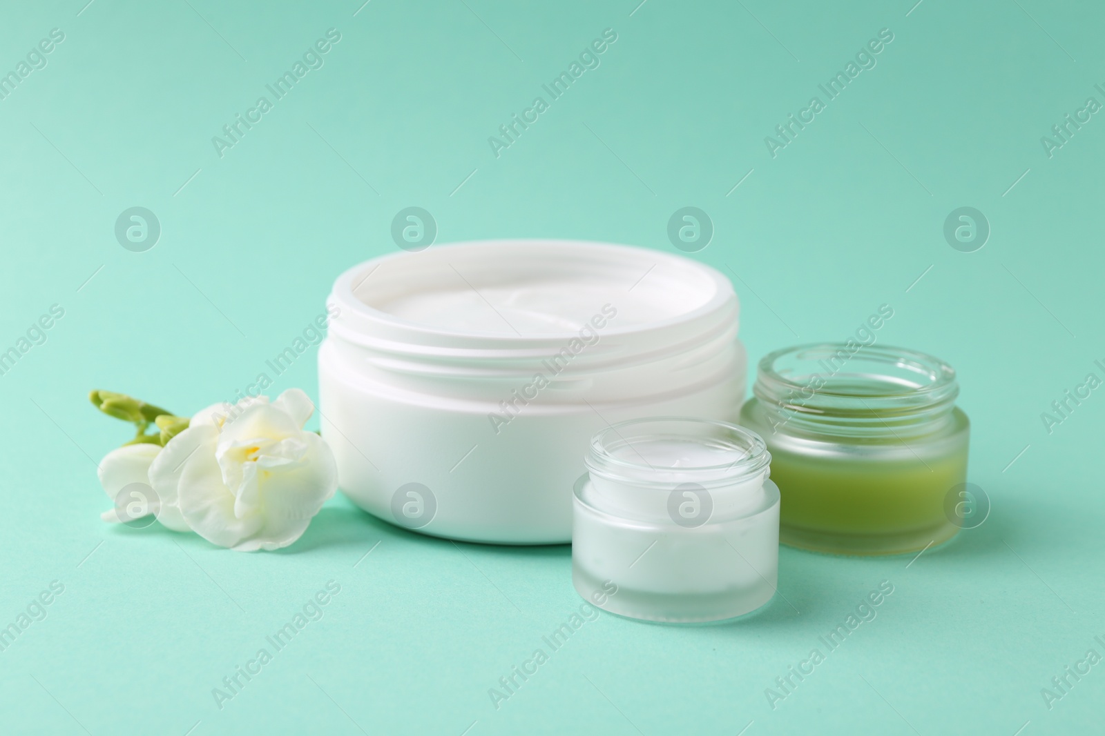 Photo of Moisturizing cream in open jars and freesia flower on turquoise background. Body care product