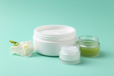 Photo of Moisturizing cream in open jars and freesia flower on turquoise background. Body care product