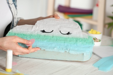 Woman decorating cardboard cloud at white wooden table, closeup. Pinata diy