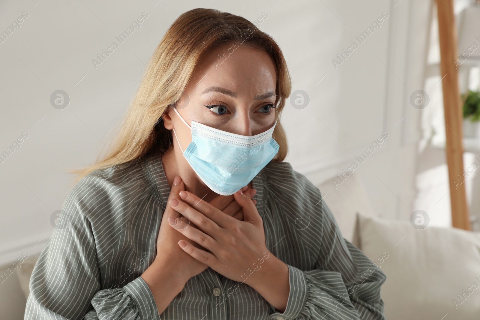 Photo of Young woman in medical mask suffering from pain during breathing at home