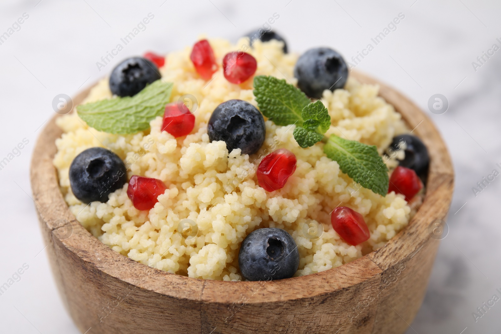 Photo of Bowl of tasty couscous with blueberries, pomegranate and mint on white table, closeup