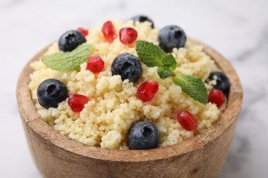 Bowl of tasty couscous with blueberries, pomegranate and mint on white table, closeup