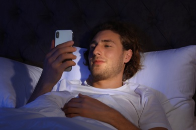 Handsome young man using smartphone in dark room at night. Bedtime