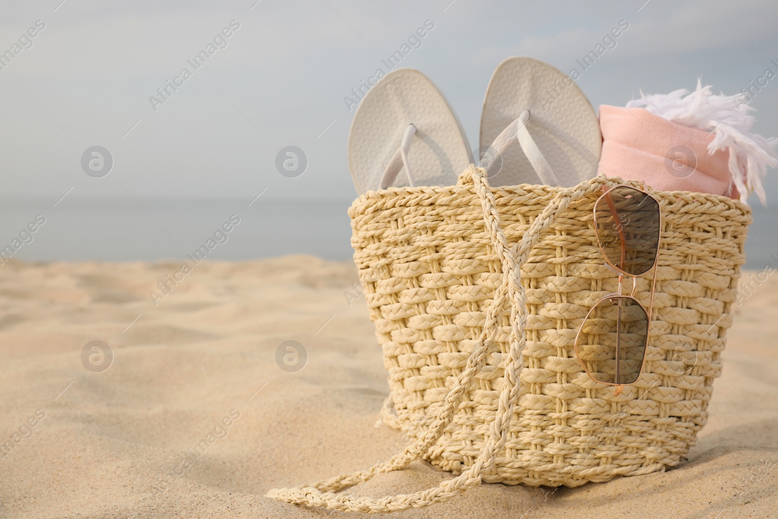 Photo of Beach bag with flip flops, towel and sunglasses on sandy seashore, space for text