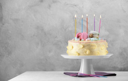 Photo of Delicious cake decorated with macarons, marshmallows and burning candles on white table against grey background, space for text