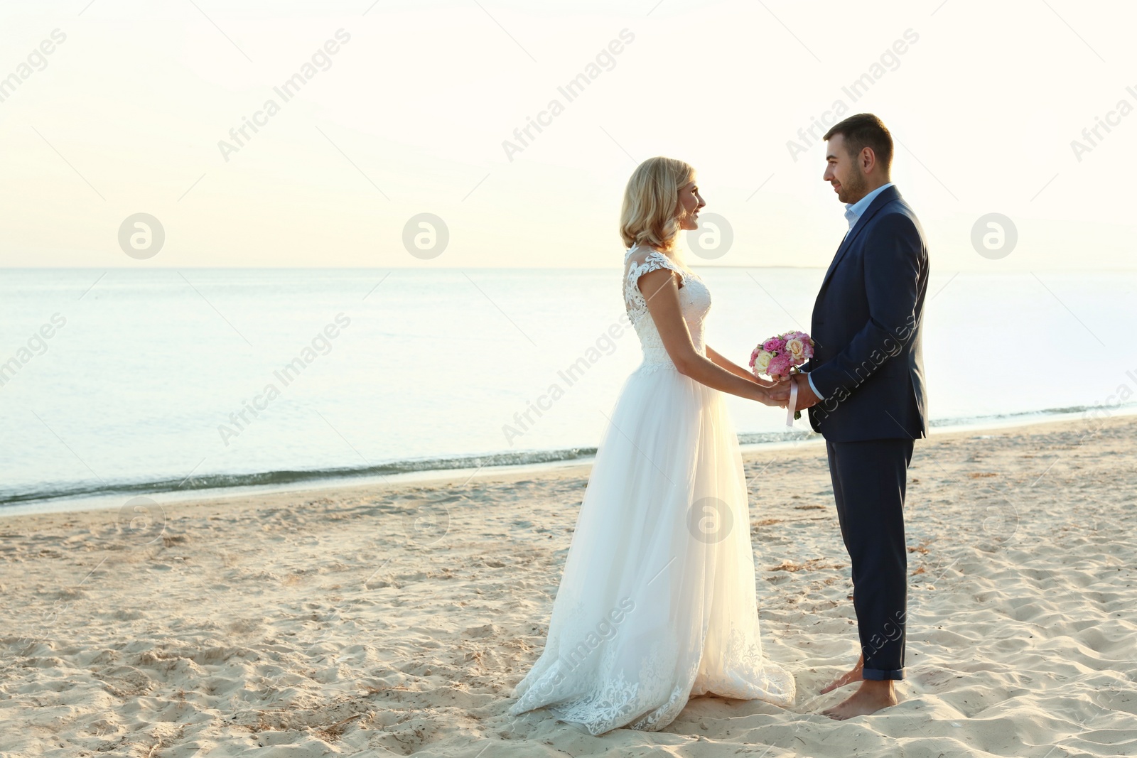 Photo of Wedding couple holding hands together on beach. Space for text