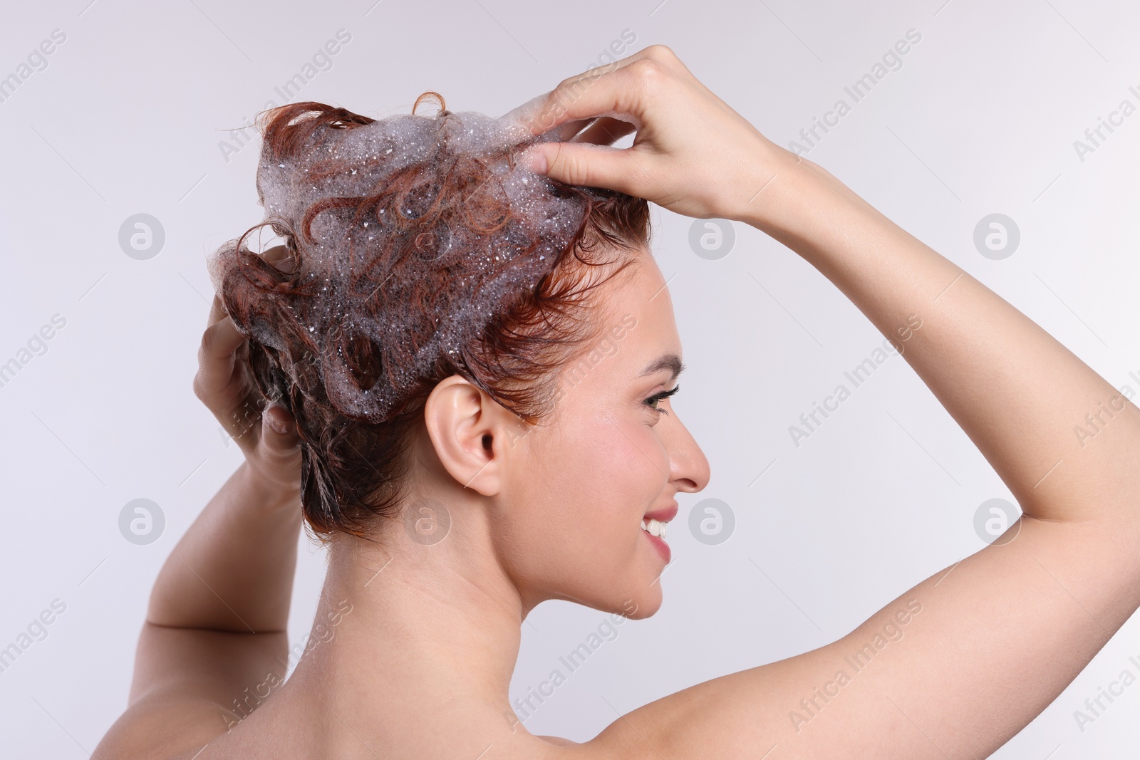 Photo of Young woman washing her hair with shampoo on light grey background, back view