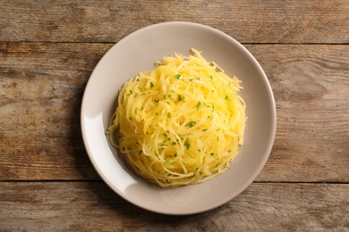 Plate with cooked spaghetti squash on wooden table, top view