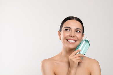 Photo of Young woman with micellar water on light grey background, space for text