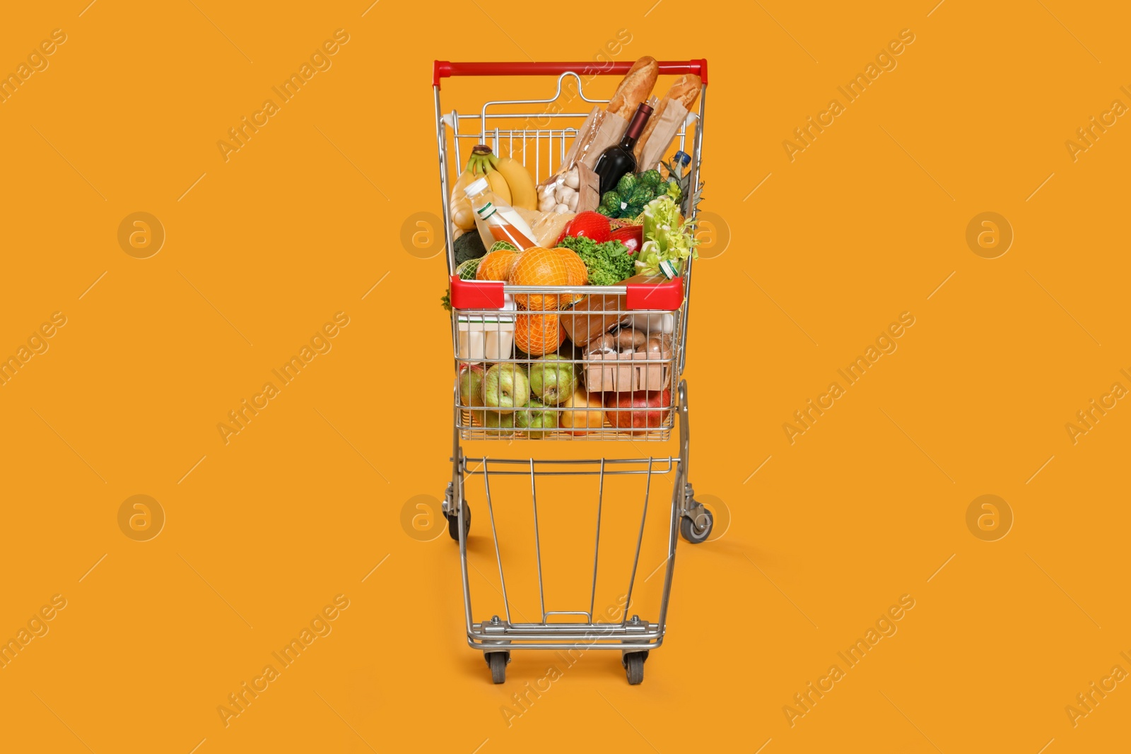 Photo of Shopping cart full of groceries on yellow background