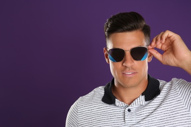 Handsome man wearing sunglasses on purple background. Space for text