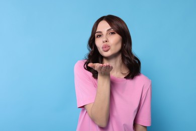 Beautiful young woman blowing kiss on light blue background