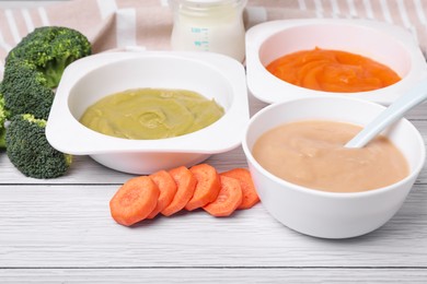 Photo of Bowls with healthy baby food and ingredients on white wooden table