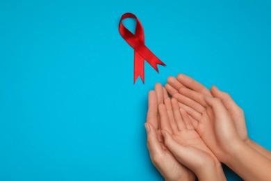Woman and girl holding red ribbon on blue background, top view with space for text. AIDS disease awareness