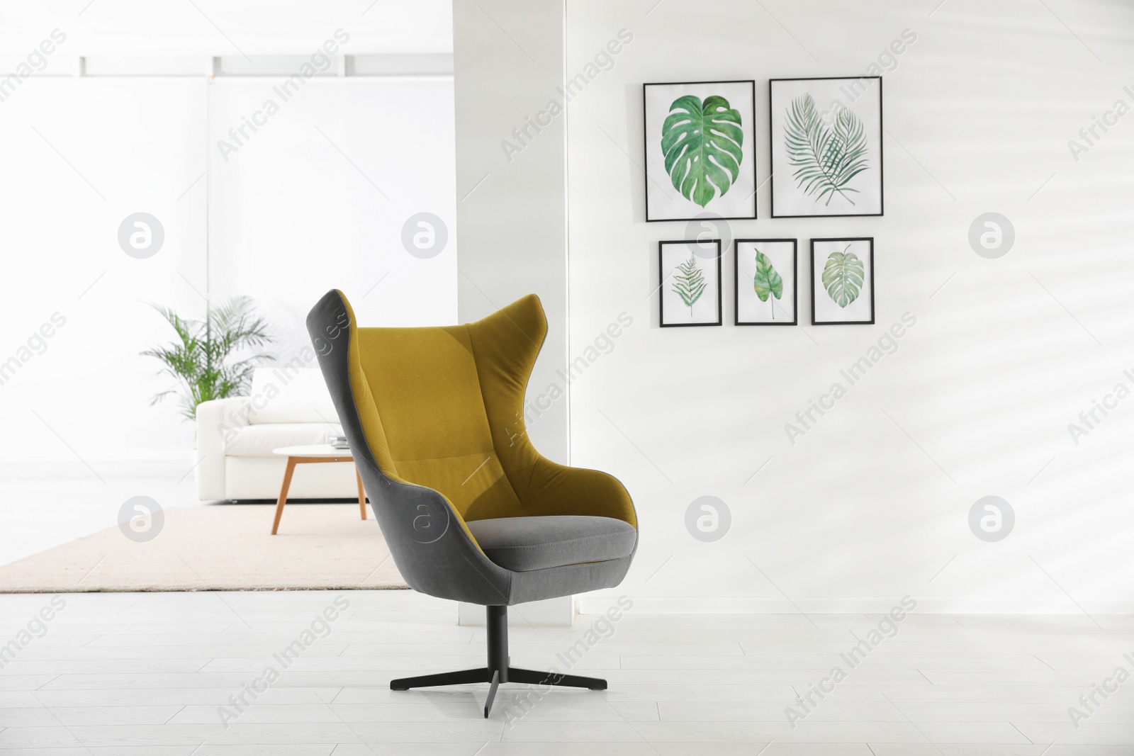 Photo of Stylish room interior with comfortable armchair and paintings of tropical leaves