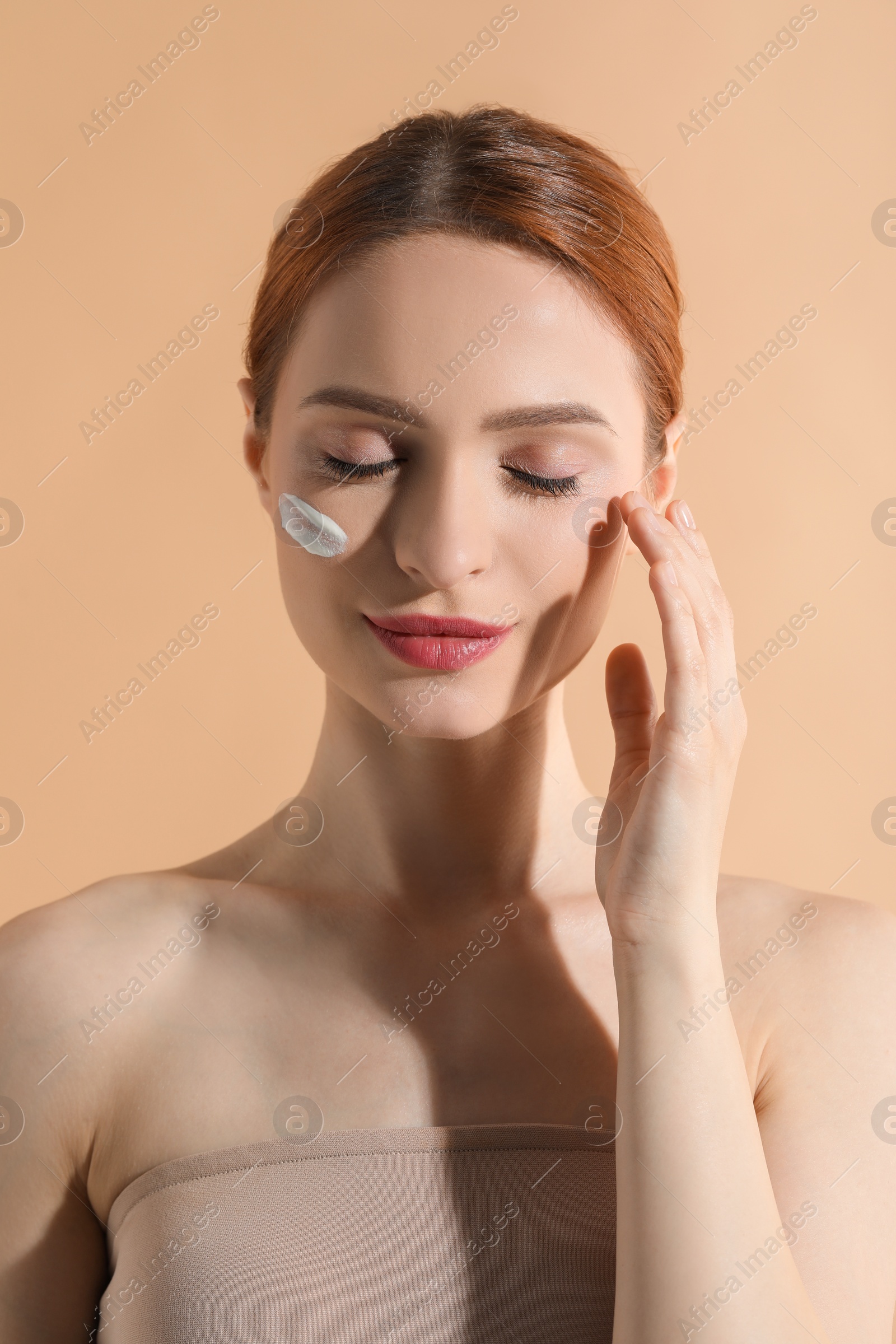 Photo of Beautiful young woman with sun protection cream on her face against beige background