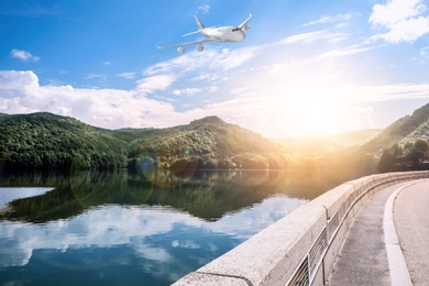 Image of Airplane flying over beautiful road along lake on sunny day