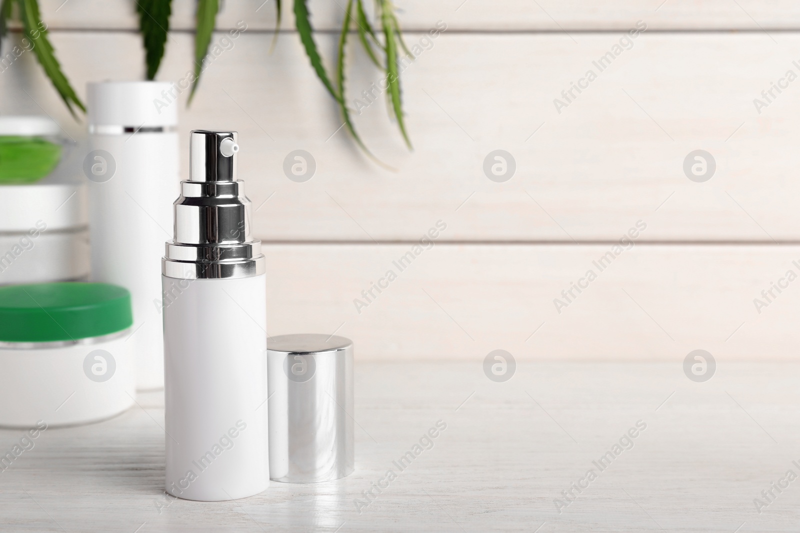 Photo of Hemp cosmetics and green leaves on white wooden table. Space for text