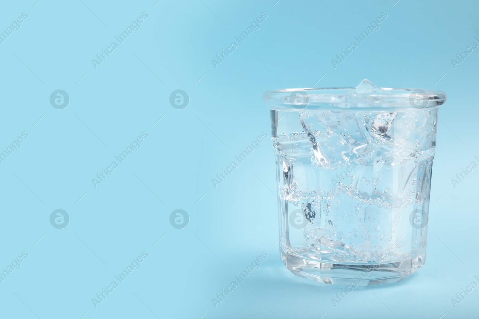 Photo of Glass of soda water with ice on light blue background. Space for text