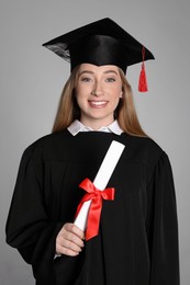 Happy student with diploma on grey background