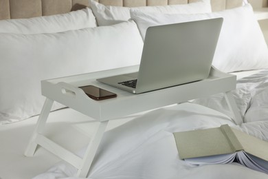 Photo of White tray with modern laptop and smartphone on bed indoors