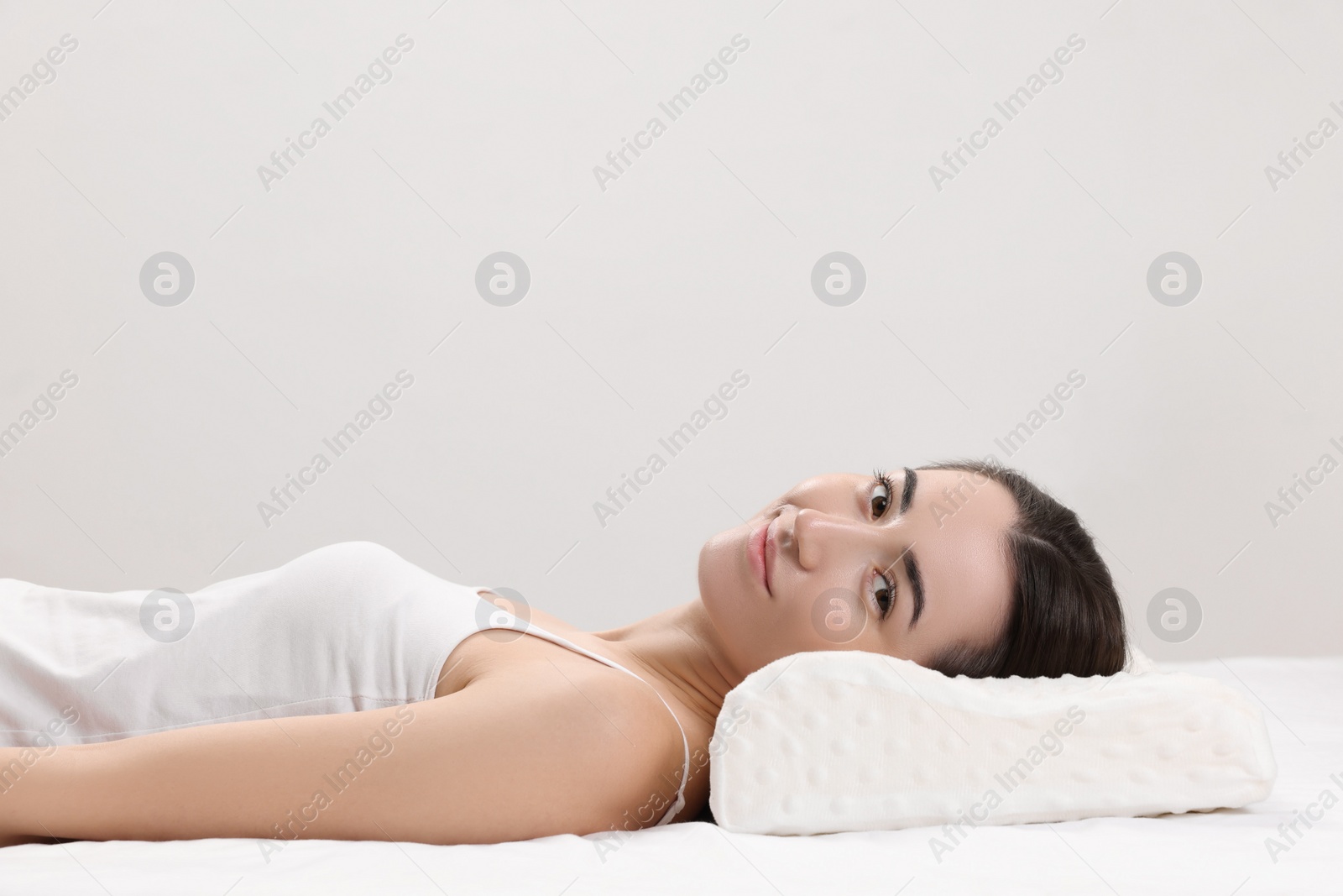 Photo of Woman lying on orthopedic pillow against light grey background, space for text