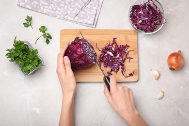 Photo of Woman cutting red cabbage on wooden board, top view