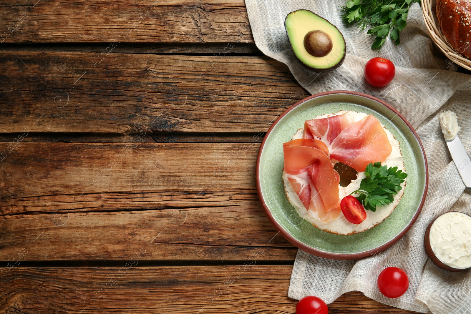 Photo of Delicious bagel with cream cheese, jamon, tomato and parsley on wooden table, flat lay. Space for text