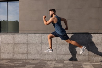 Photo of Young man running near building outdoors. Space for text