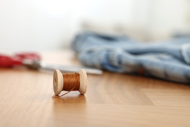 Photo of Spool of brown thread on wooden table, space for text