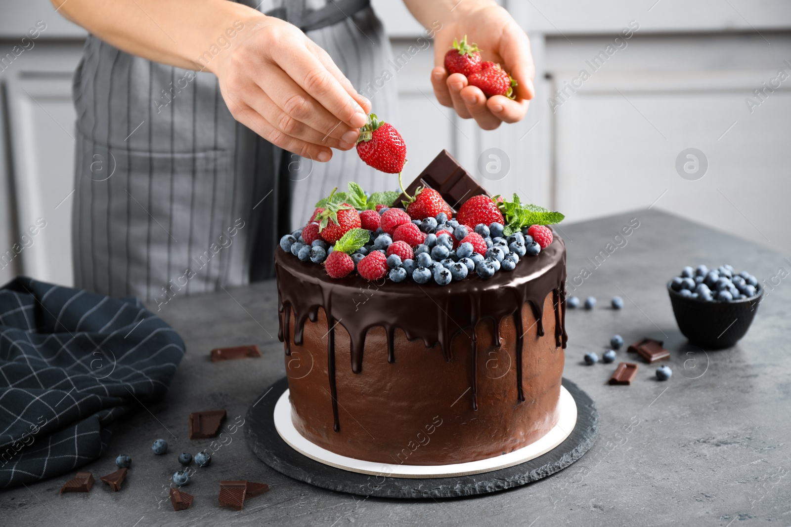 Photo of Woman decorating delicious chocolate cake with fresh strawberries at table, closeup