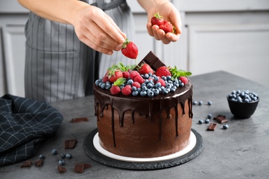 Woman decorating delicious chocolate cake with fresh strawberries at table, closeup